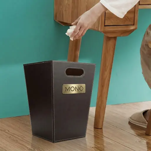 Open Top Pu Leather Waste Basket — DBN-1047 — A 16L square open-top waste basket with a wooden frame wrapped in premium PU leather and a non-woven lining. Ergonomic arc handles make it easy to carry and empty, while the non-slip, wear-resistant base protects floors. Refined stitching and a 19x24.7x35cm form suit elegant guest rooms, available in black, white or brown.
