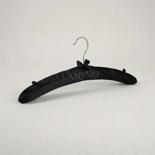 Satin Padded Hanger With Holder — HNG-1029 — A satin-padded hanger with a non-slip rubber-covered hook that protects delicate garments from marks and creases. A chrome holder adds a refined touch for guest wardrobes, with a strong, durable build. Supplied 200 pieces per carton, measuring 38cm wide, in black or white.